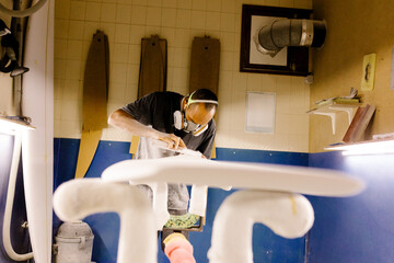 Entire figure of a craftsman manually sanding a newly made surfboard