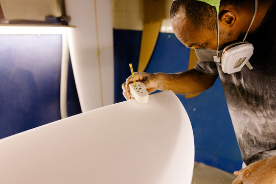 Craftsman using a pencil to mark the correct shape of a new surfboard
