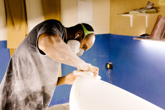 Surfboard craftsman using sandpaper to hand-shape a newly built board