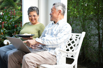 Happy senior couple using laptop together at home garden, Elderly asian couple enjoying retirement life with technology outdoors, Active aging lifestyle seniors sharing digital moments at home