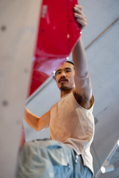 Climber in Indoor Gym Reaching Red Hold During Rock Climbing Session