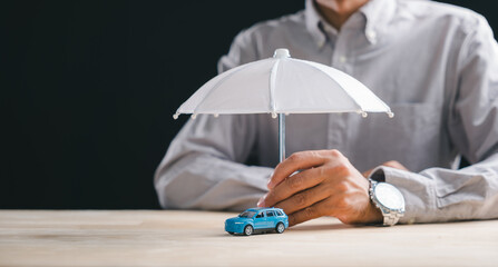 Car insurance concept features person hand holding umbrella over blue toy auto, demonstrating strong vehicle protection, safety for driver, smart finance plans, and accident claim cover