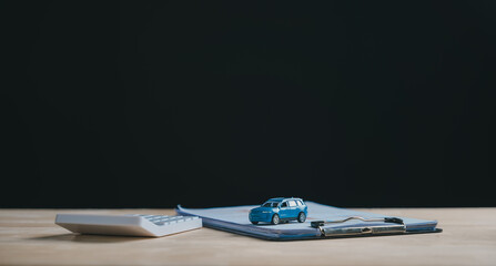 Blue miniature car rests on finance document, outlining terms for auto loan and purchase, calculator stands nearby, representing costs for car contract, lease, sale, or insurance at dealership