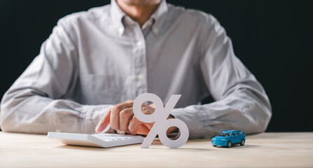 Person working on calculations for car interest rate, pressing buttons on calculator, miniature auto model rests near prominent percent sign representing finance loan options and sale