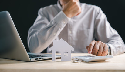 Man focusing on financial planning for home property, using calculator and laptop to determine mortgage loan, keys represent new house estate investment