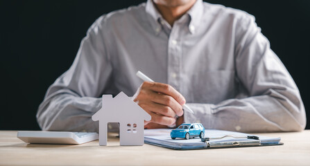 Person signs car and home contract, document details loan insurance policy paperwork, considering property and auto registration business plan with calculator on desk