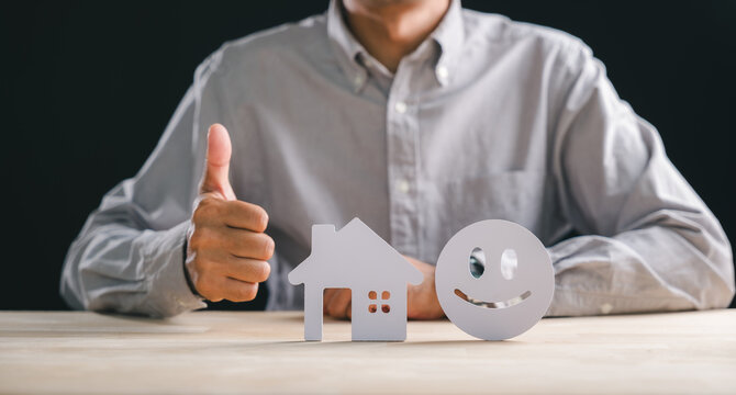 Home customer satisfaction review concept, person shows thumbs up near house shape and smiley face, symbolizing best real estate property feedback and service five star rating