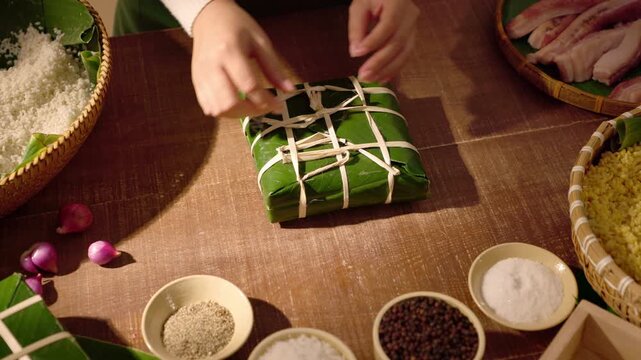 Cinematic shot of hands wrapping traditional Chung cake with dong leaves and raw ingredients, capturing Vietnamese Tet cooking rituals and Lunar New Year food heritage