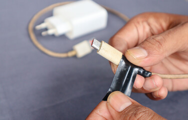 Fototapeta premium Close-up of handyman male applying insulating tape to frayed charging cable, demonstrating simple DIY repair technique for damaged electronics.