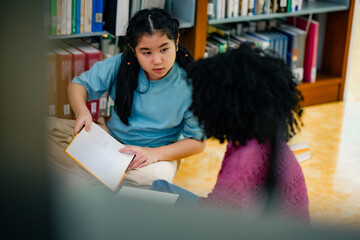 Schoolchildren enjoying reading activity on library floor surrounded by books. Natural interaction highlights learning motivation literacy skill diversity friendship supportive school culture.