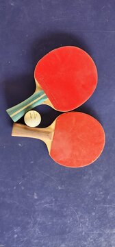 A pair of table tennis paddles and a ball, placed on a blue background
