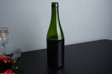 Wine bottle and glass on black wooden table as Christmas festive holiday decoration. Blank background mockup with copy space for adding text, logo, product, or promotional design.