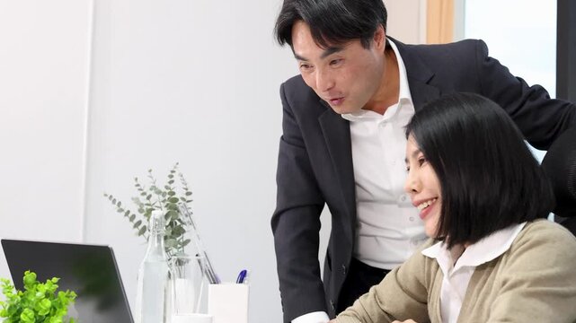Asian Business Manager and Employee Collaborating on Laptop in Modern Office