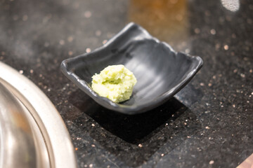 Green wasabi paste in a black ceramic dish. Close up