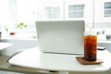Iced black coffee in a glass on a modern office desk with laptop, refreshing drink for workspace at cafe