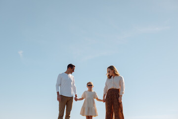Candid family moment outdoors: parents and daughter holding hand