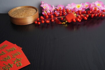 Empty background of a dark wooden tabletop with cherry blossom decorations, a bamboo dimsum steamer, and an empty plate for Chinese Lunar New Year celebration.