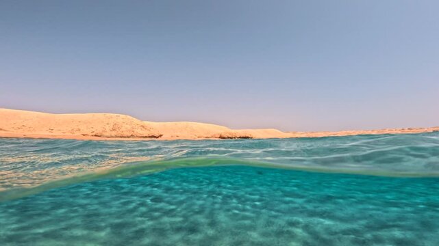 Half underwater slow motion seascape with sandy seabed and rolling waves near desert coast