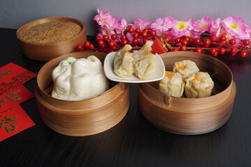 Various steamed dim sum such as jiaozi, baozi and shumai on woven bamboo steamer isolated on dark black wooden table background. Steamed dumplings for Chinese New Year party.
