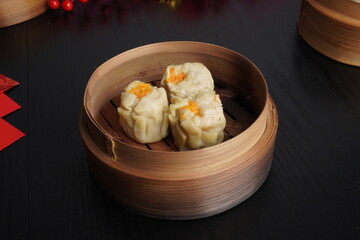 Steamed shumai dim sum on wooden bamboo steamer plate isolated on dark black wooden table background. Steamed dumplings for Chinese New Year party.