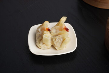 Steamed shumai dim sum on white plate isolated on dark black wooden table background. Steamed dumplings for Chinese New Year party.