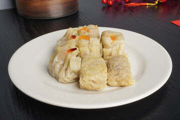 Steamed shumai dim sum on white plate isolated on dark black wooden table background. Steamed dumplings for Chinese New Year party.