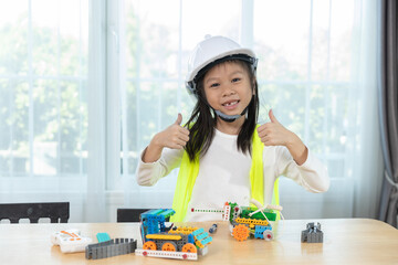 Smiling young girl wearing hard hat and safety vest giving thumbs up beside her robotic inventions, representing STEM success, engineering confidence, creative learning for kids.