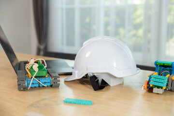 White safety helmet placed on desk with colorful robotic kits and laptop, representing STEM education, engineering learning tools, Innovation for kids and classrooms.