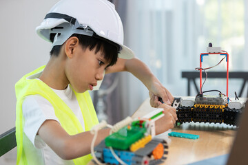 Boy wearing hard hat with safety vest assembling a robotic car, representing STEM education, engineering skills, early learning in robotics and innovation for kids.