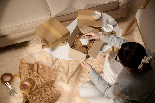 Woman packing a mug in a cardboard box with protective paper