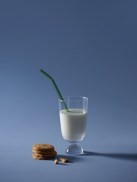 Glass of milk with a green straw and cookies on a blue background