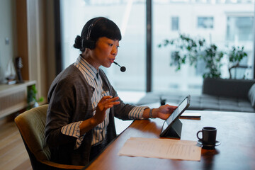 Asian woman working remotely on video call using tablet

