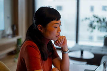 Asian woman thinking while working on laptop
