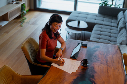 Woman working remotely from home signing documents on table
