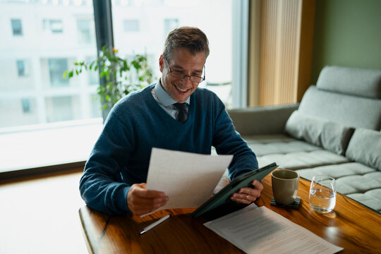 Mature man smiling while reading document at home office
