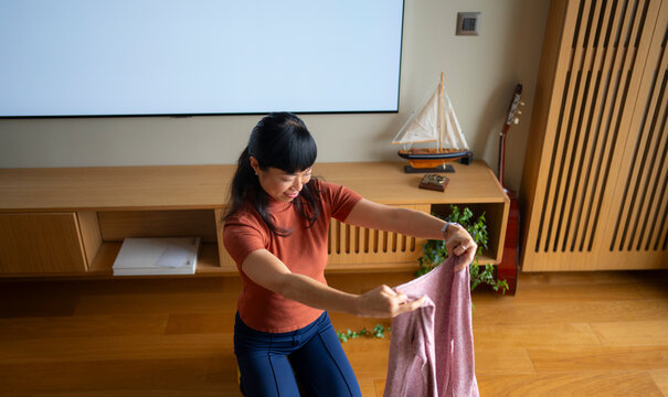 Asian woman folding laundry on living room floor

