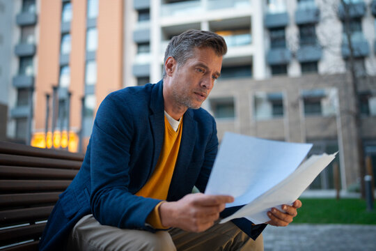 Mature man reading business documents outdoors in city
