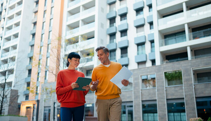 Real estate agents discussing project outdoors using tablet on buildin