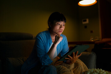 Woman watching drama or suspense movie on tablet at night
