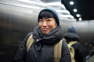 Woman riding elevator up with a happy expression
