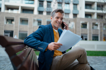 Businessman talking on phone reading documents urban park
