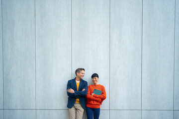 Business colleagues standing against modern blue wall outdoors
