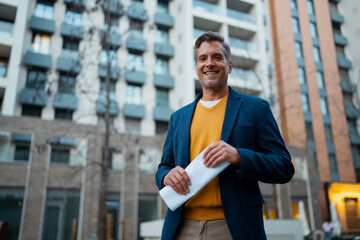 Confident man smiling outdoors holding documents in urban setting
