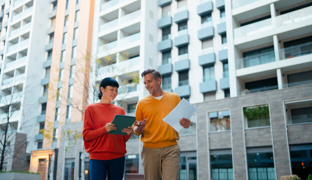 Real estate agents discussing project outdoors using tablet on buildin