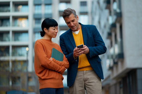 Diverse business colleagues reviewing smartphone content outdoors
