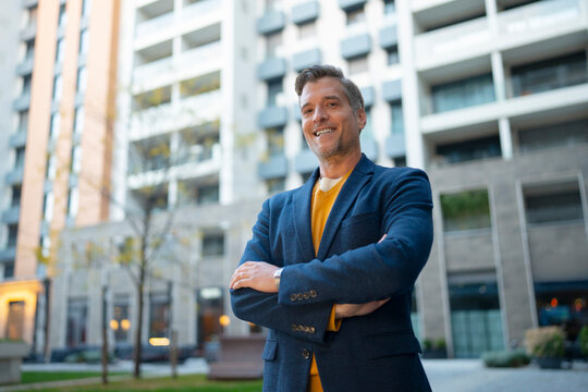Smiling confident businessman standing with crossed arms in city
