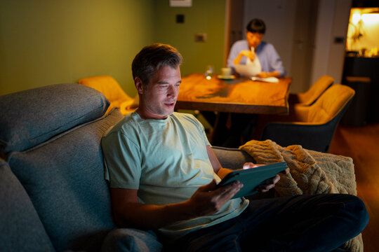 Man relaxing on sofa using digital tablet at home
