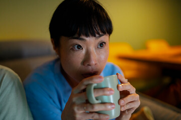 Woman intently watching television show while drinking hot beverage
