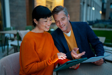 Diverse business colleagues discussing project on tablet outdoors
