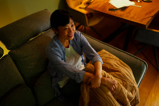 Asian woman relaxing on sofa watching evening entertainment
